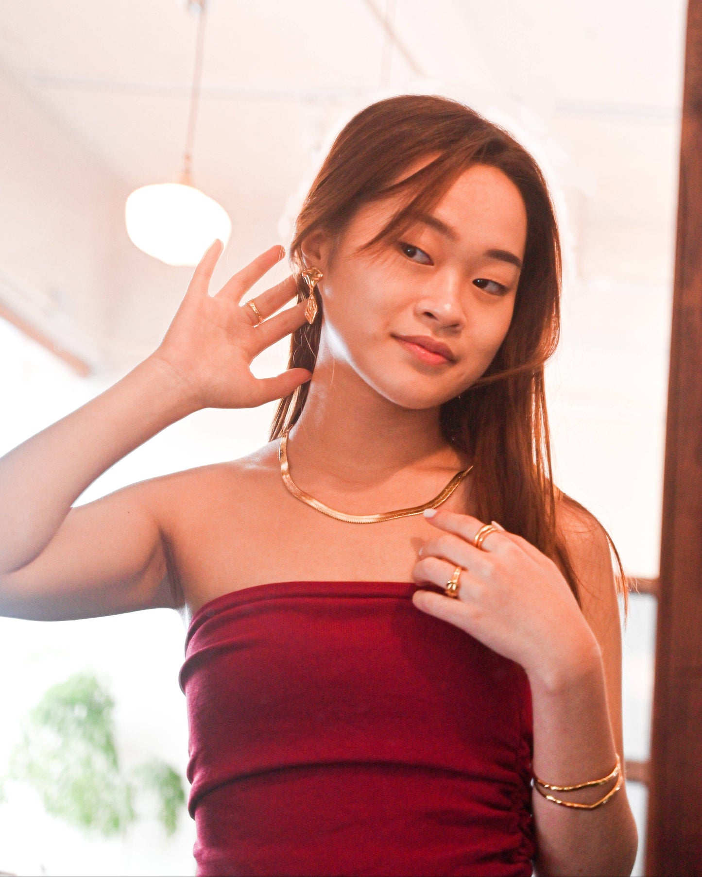 A woman in off-shoulder red top wearing the 18K Gold Herringbone Necklace and looking into the mirror to pose