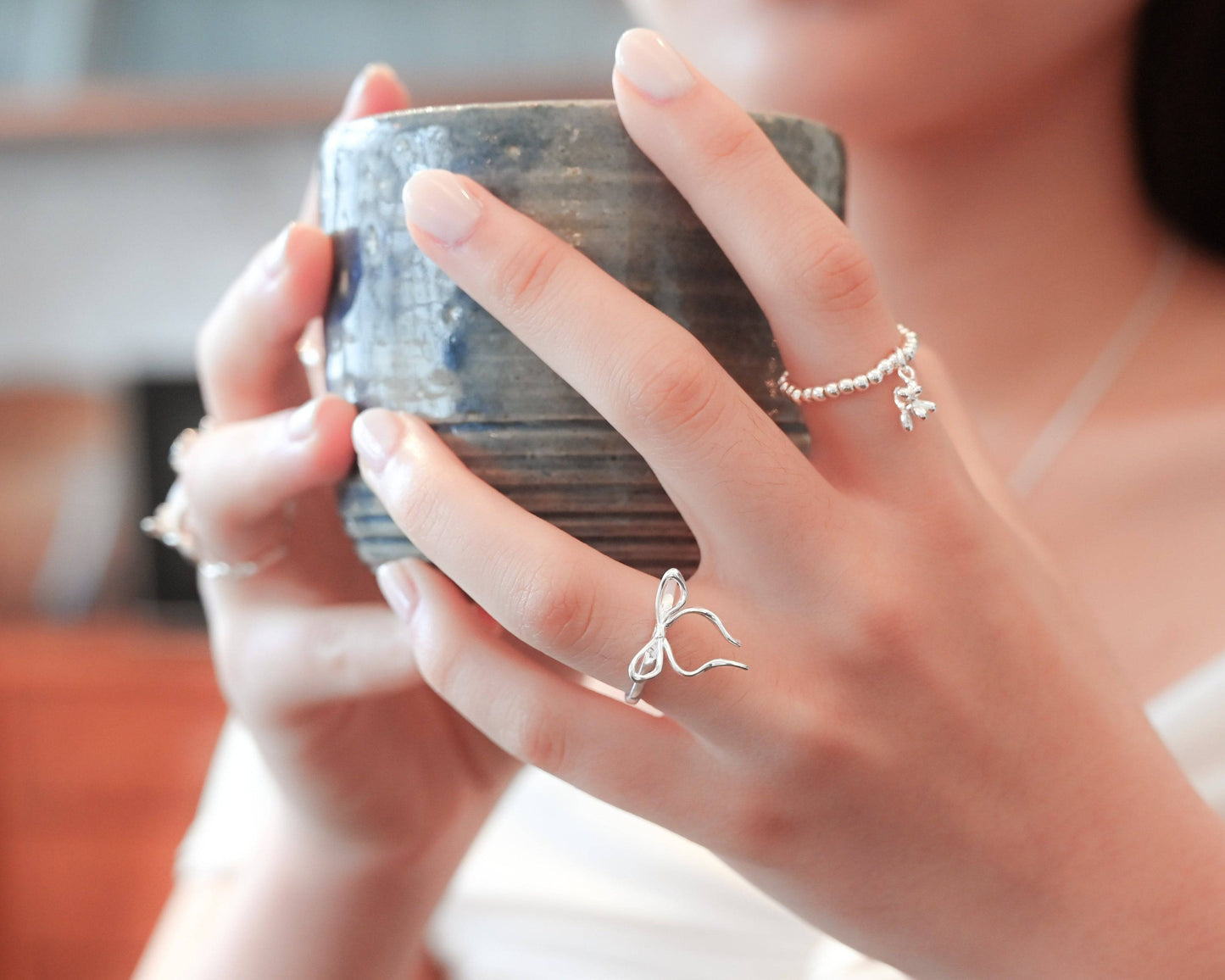 A woman in white off-shoulder top wearing the Thin Bow Tie Ring and holding a blue ceramic cup