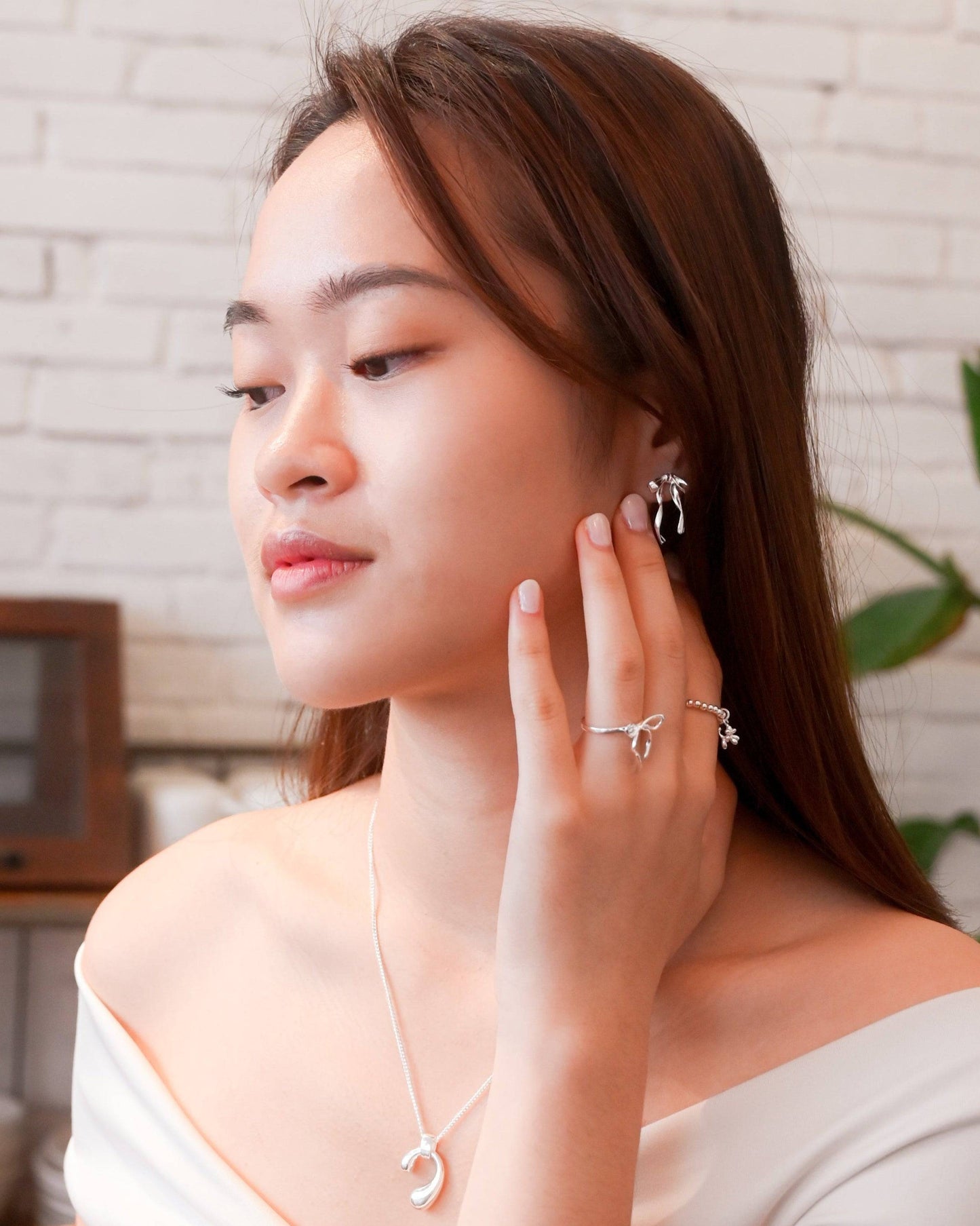 A woman in white off-shoulder top wearing the Thin Bow Tie Ring and posing peacefully