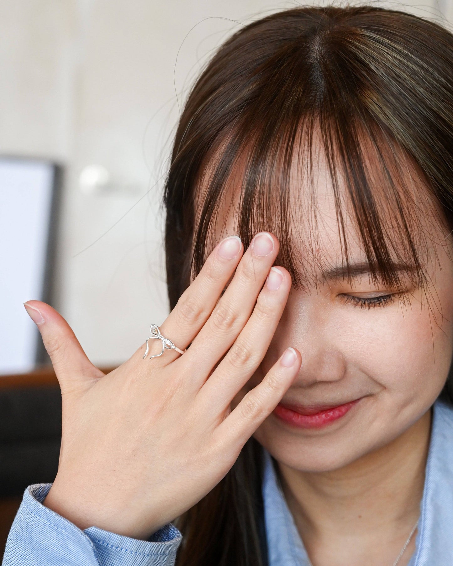 A woman in blue shirt wearing the Thin Bow Tie Ring and cover half of her face happily