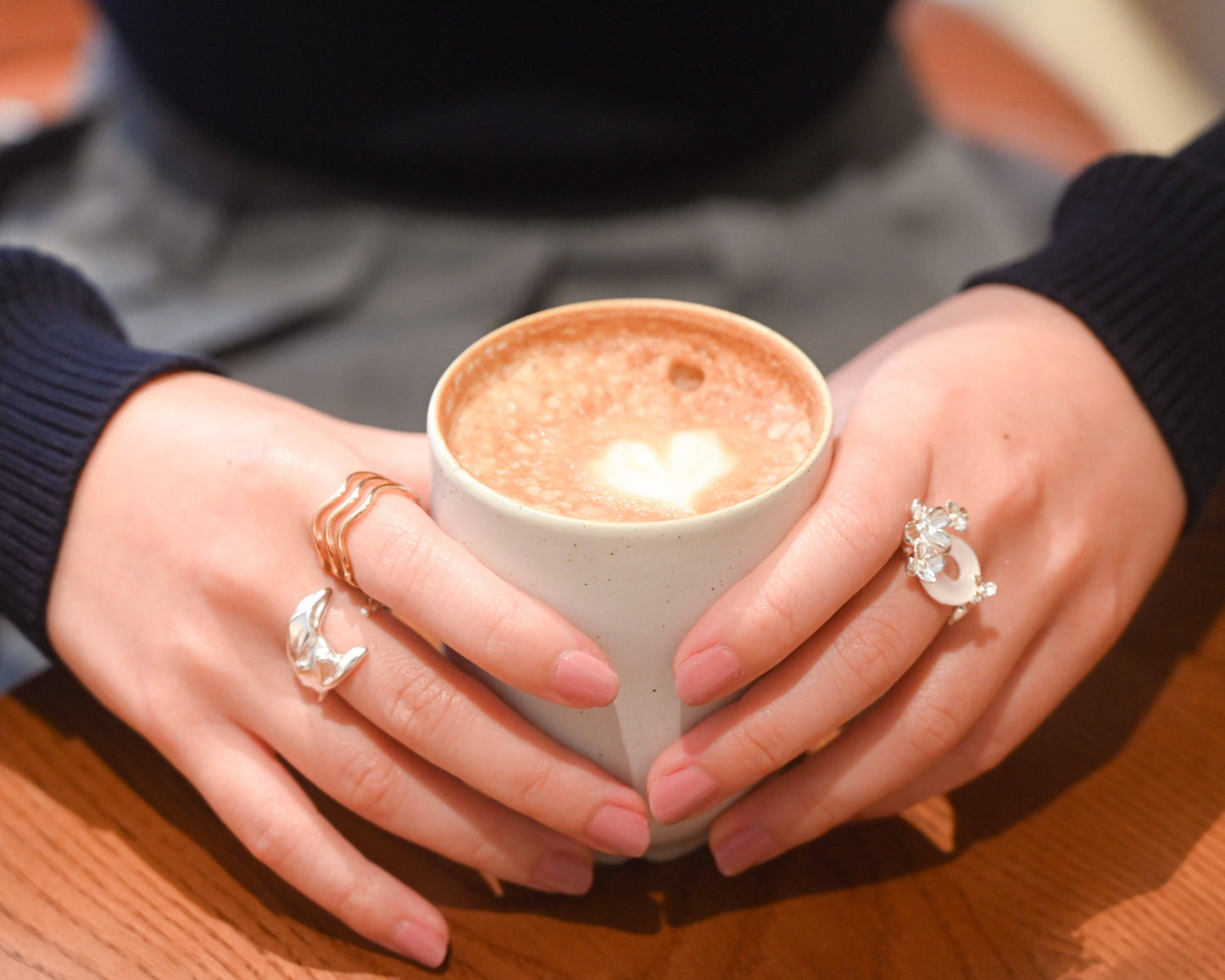 A woman in navy blue sweater wearing the Sterling Silver Whale Tail Ring and holding a cup of latte
